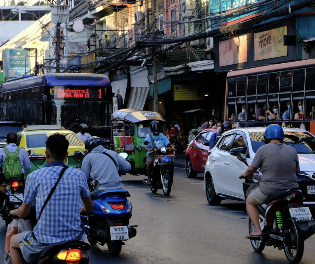 A busy road in Bangkok, Thailand with mopeds, cars and an electric bus