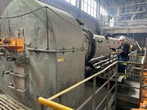 A man with a thermometer is monitoring the temperature of a furnace for cement making.