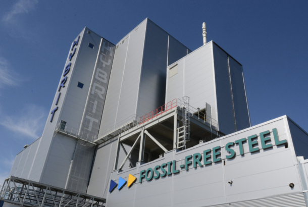 A view looking up at the HYBRIT fossil free steel pilot plant in Luleå, Sweden. A grey building with a very blue sky behind.