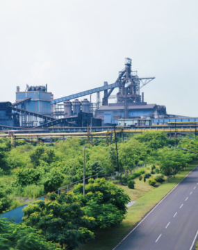 A steel plant in the background with an area planted with trees in front of it. The location is India.