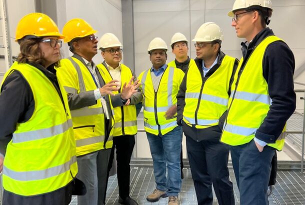 a group of people in yellow high viz vests and hard hats are talking in a factory.